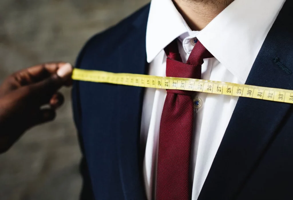 Traje de novio, sastre revisando y tomando medidas al cliente para arreglos de traje a medida.