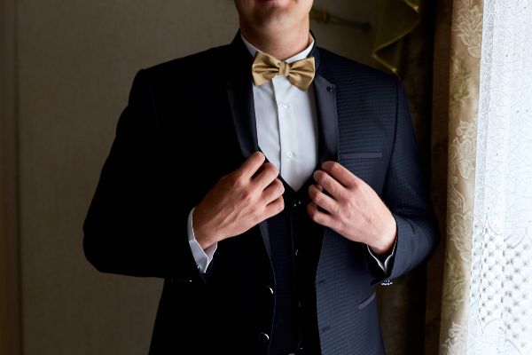 Smoking hombre elegante, sostiene abrigo de traje clasico hecho a la medida.