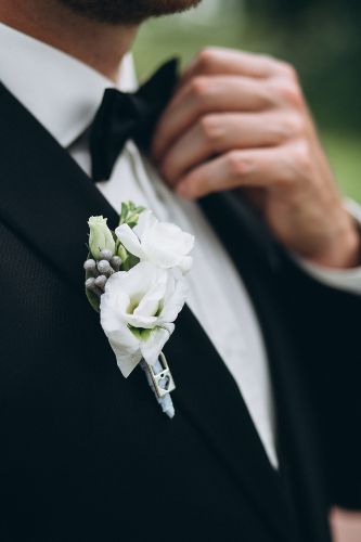 Trajes de novio; traje negro con moño y flor blanca